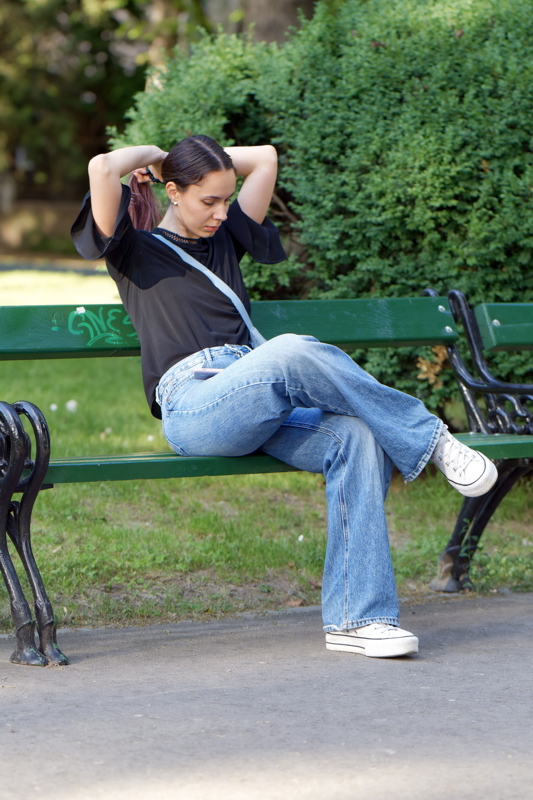 1 - Girl wearing a relaxed, modern outfit combining elements of casual streetwear and feminine details, sitting on a bench